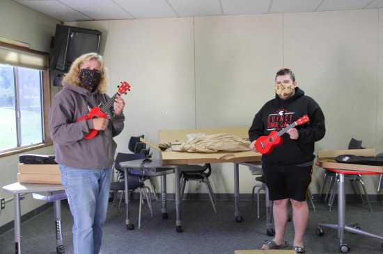 PUSD teacher Mrs. Brown receives ukuleles from QHS senior Tristan McMichael. Photo shows them holding instruments and wearing masks.