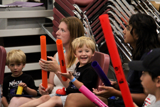 A young boy smiling and playing a boomwhacker during the summer music program